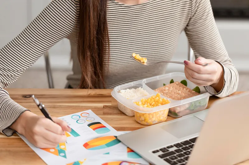 Colaboradora almoçando refeição saudável enquanto trabalha no notebook